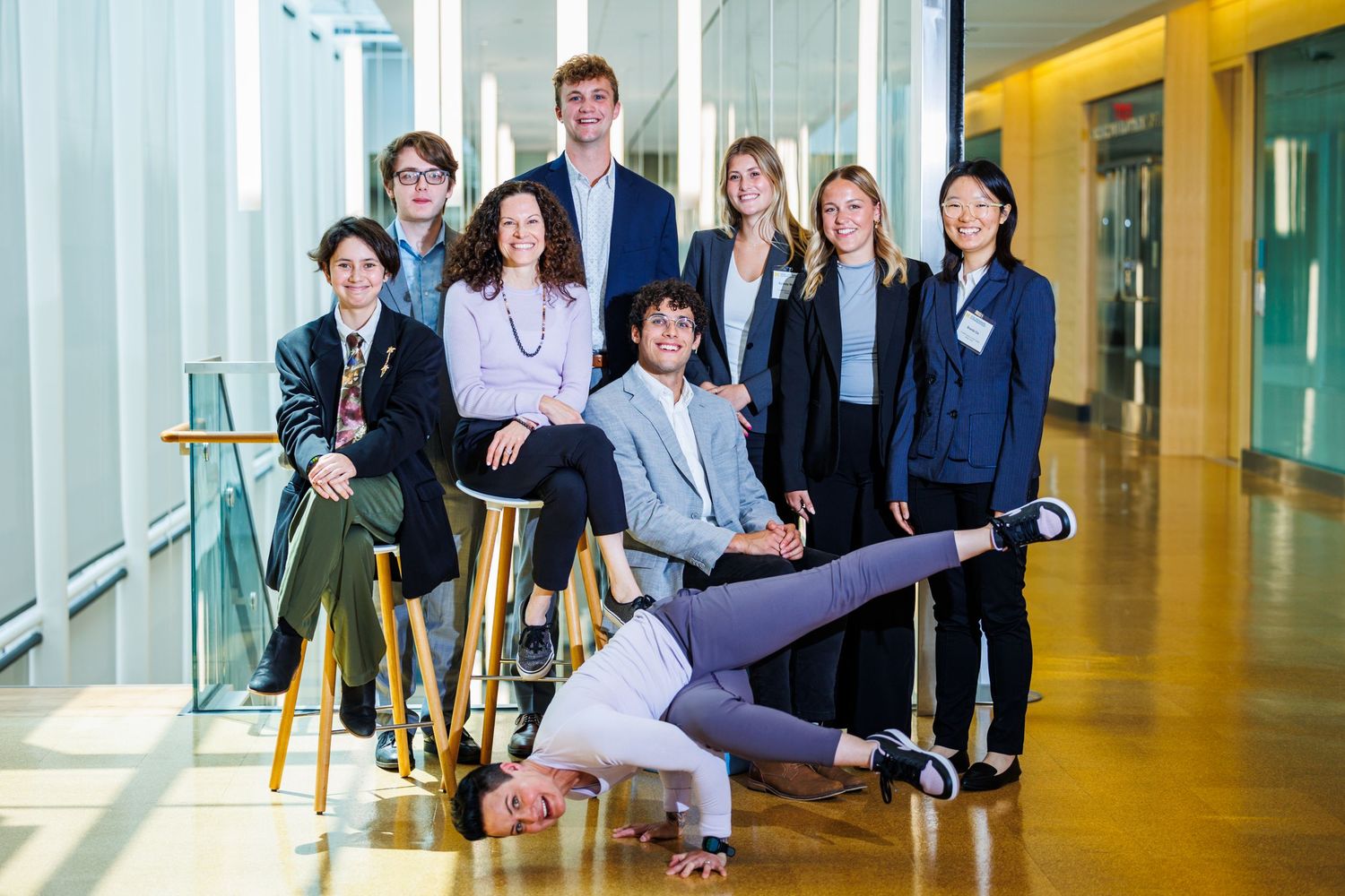 Group of young professionals posing playfully in modern office corridor.