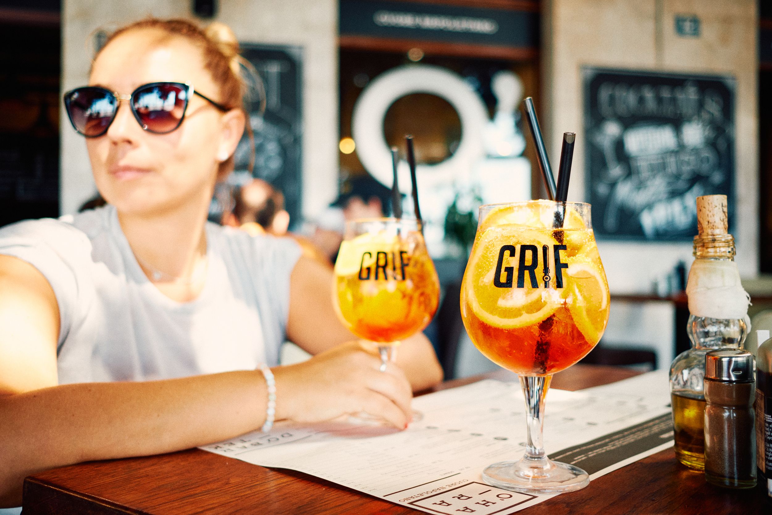 Two orange aperitif cocktails with straws on a wooden table at a cafe.