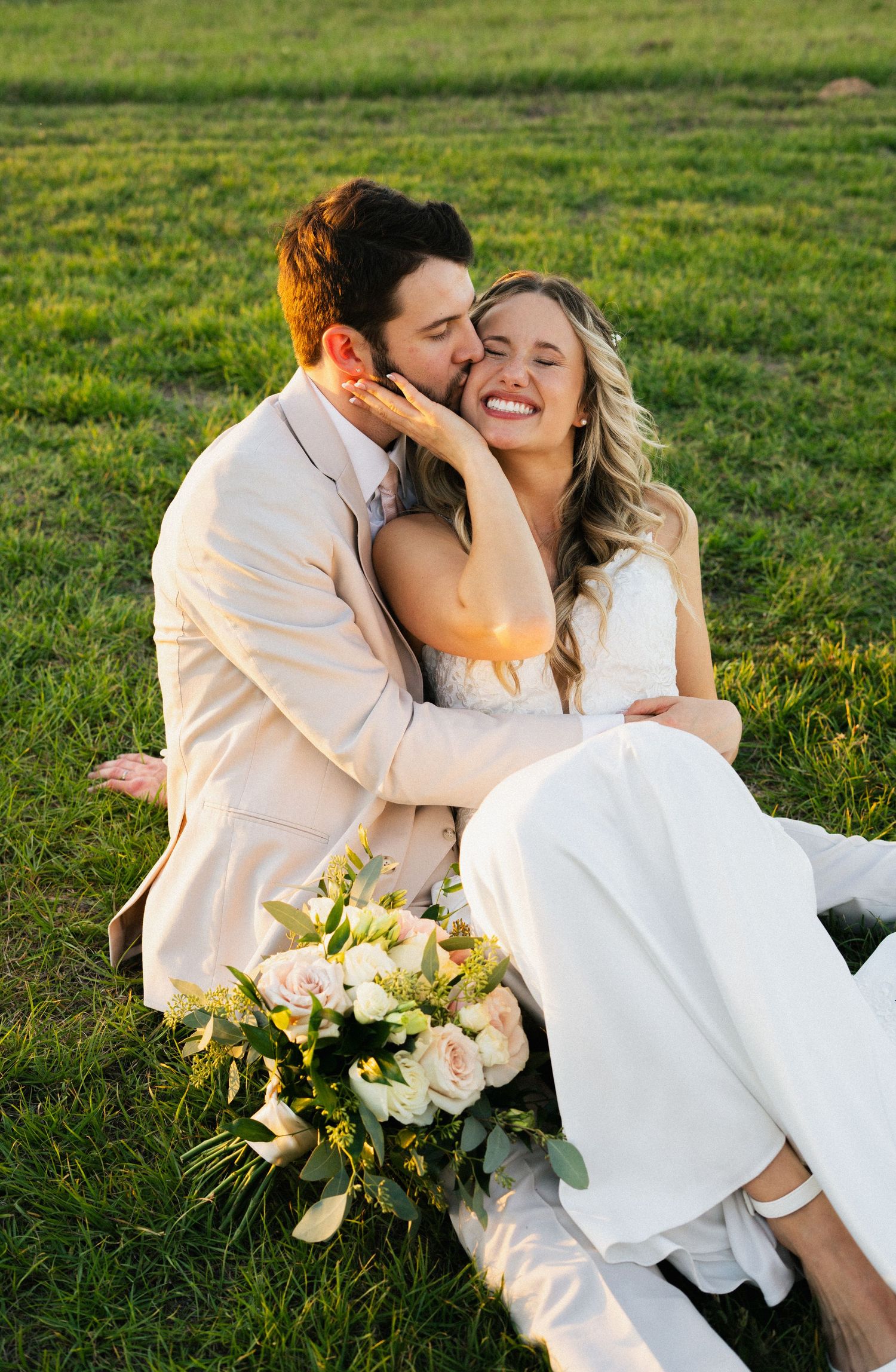 A couple shares a tender moment on grass with white flowers at sunset.