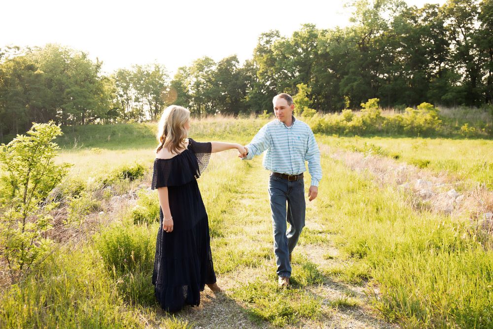 A couple holds hands while walking through a sunlit summer meadow.