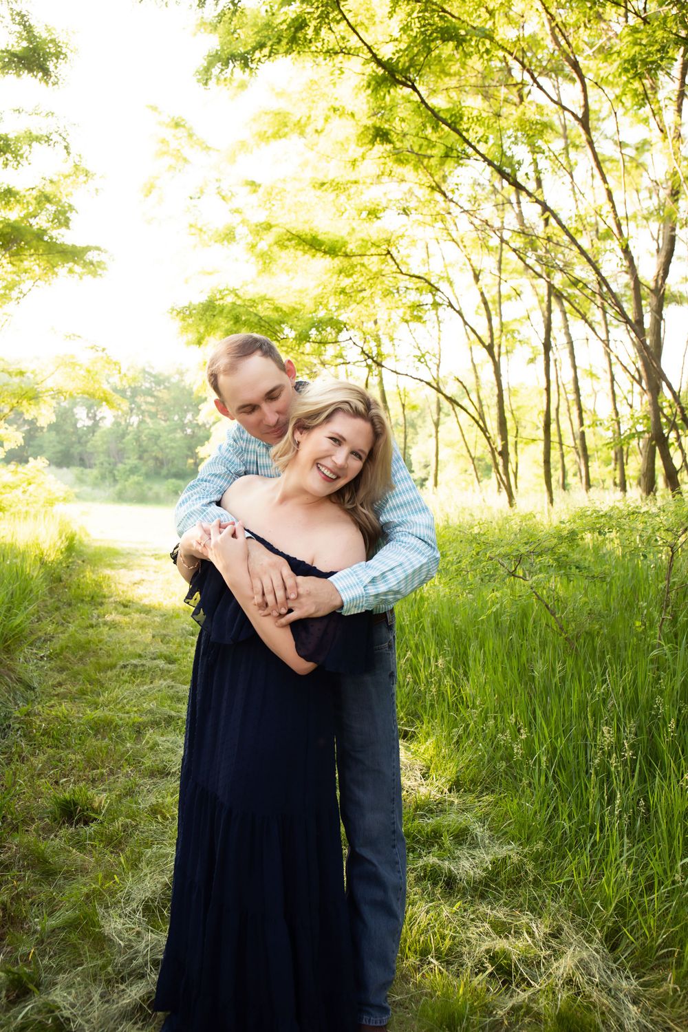 A couple shares an embrace in a sunlit forest clearing with golden leaves overhead.