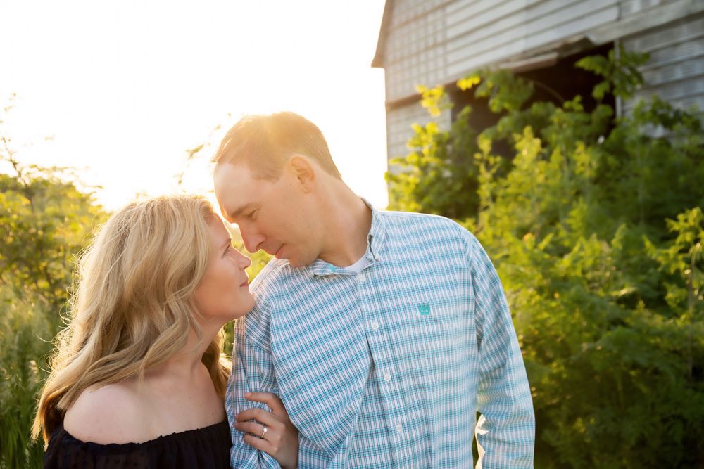 A couple shares an intimate moment in front of a rustic barn during golden hour.