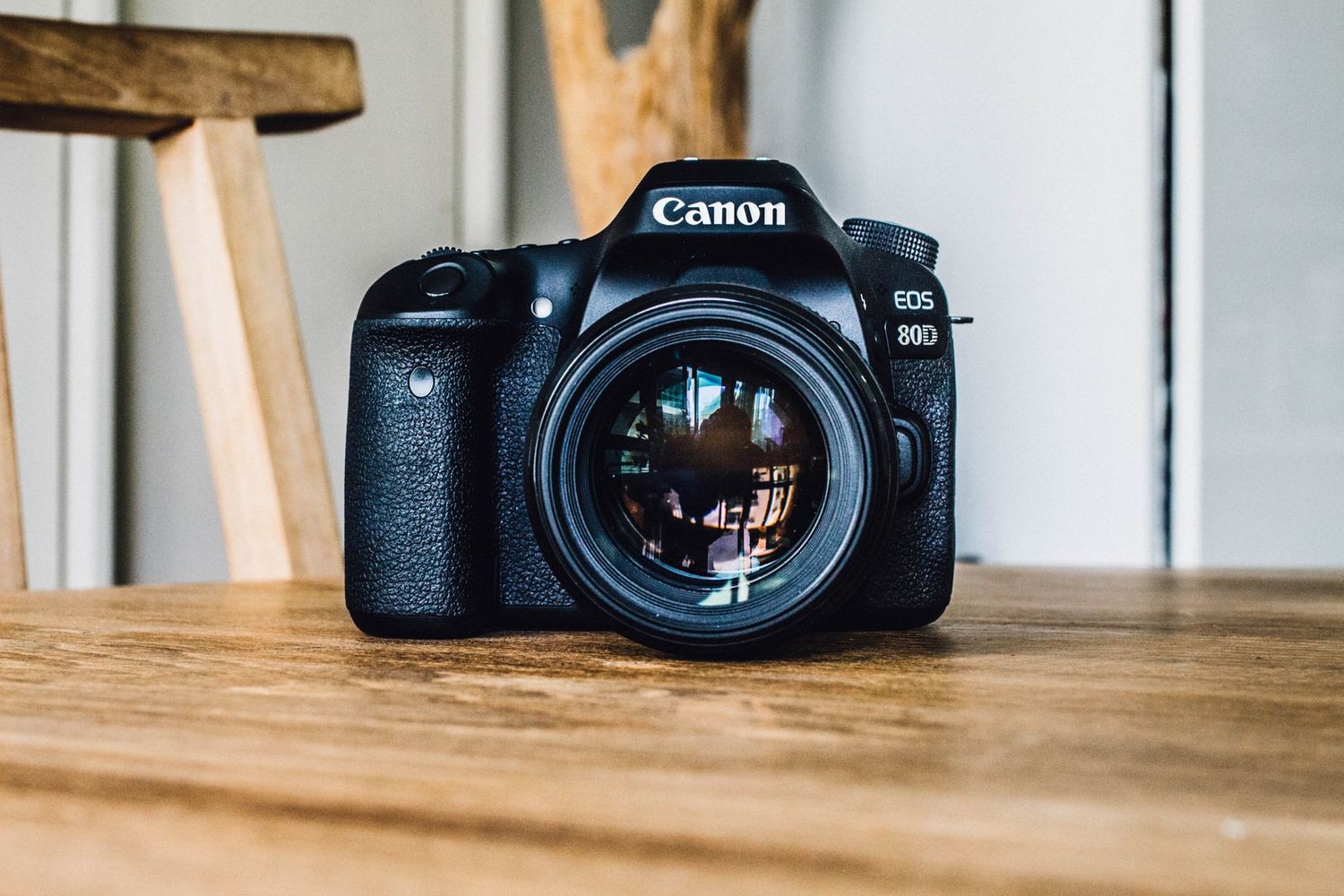 Canon DSLR camera with lens sits on wooden table surface.
