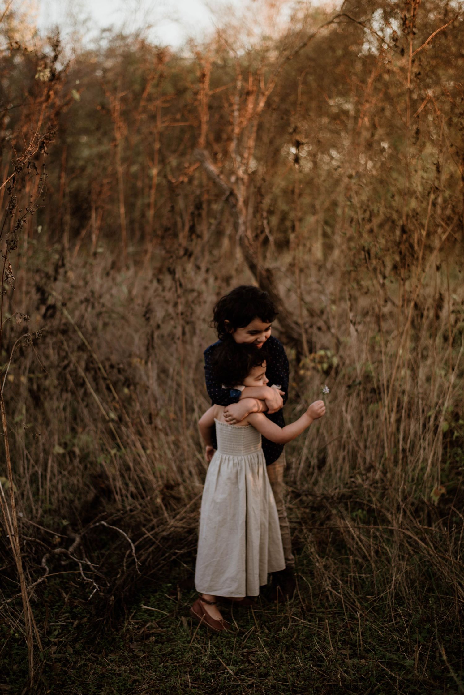 Tender family moment captured in tall grass during sunset.