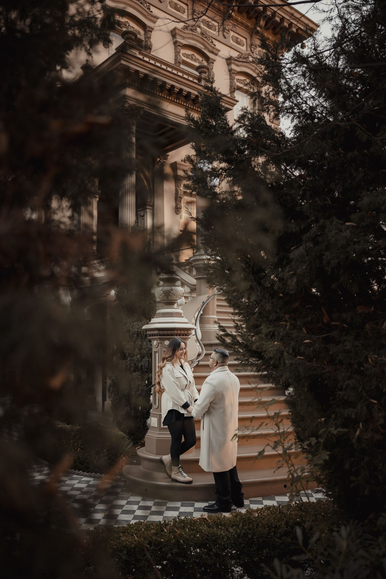 A couple poses on grand stone steps of an ornate historic building.