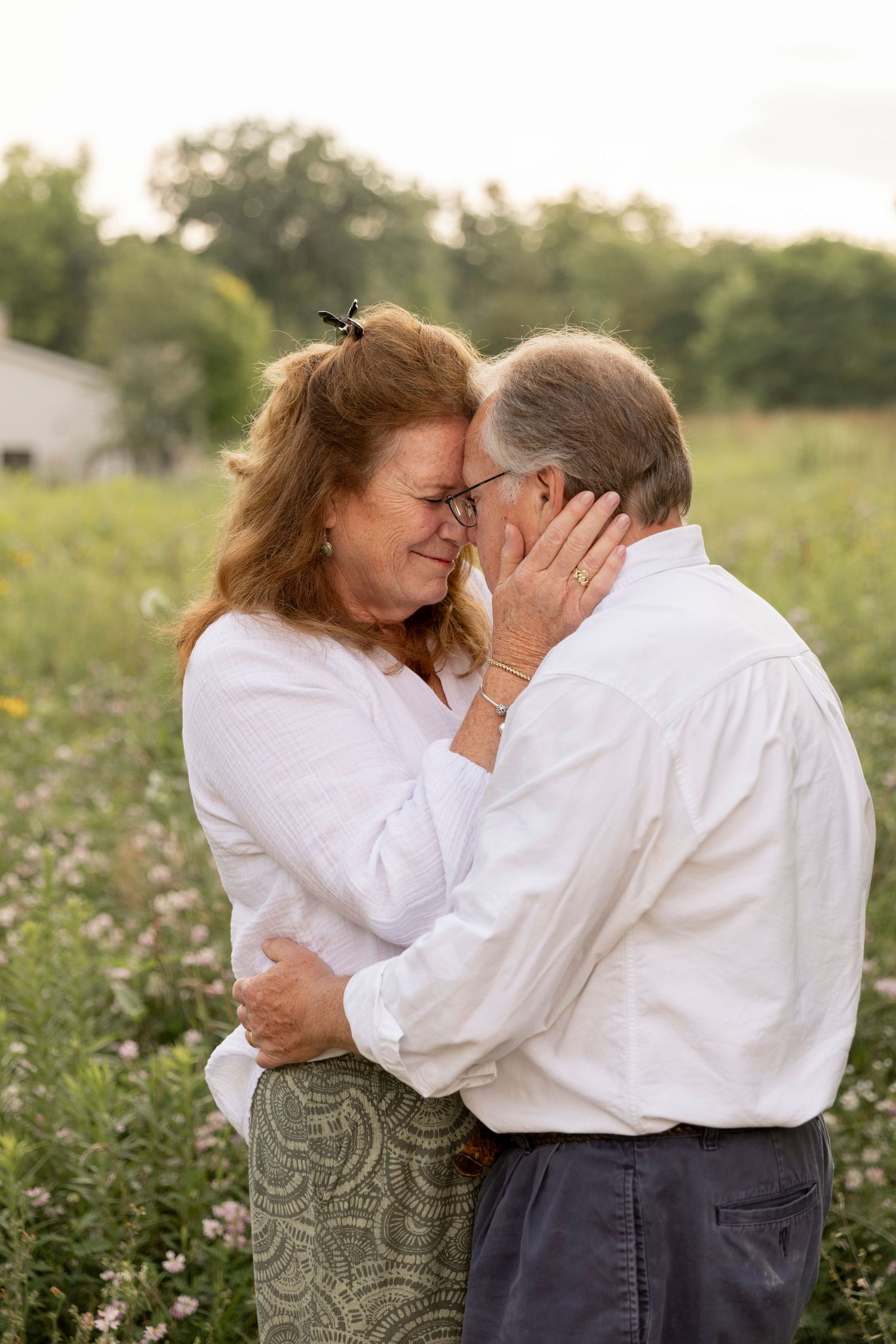 couple wearing white standing in a field holding each other close