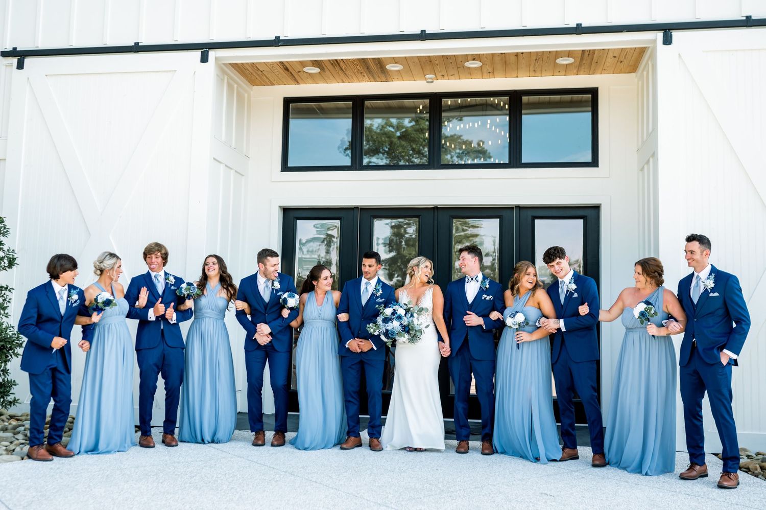 Wedding party lined up against modern white building with black windows.