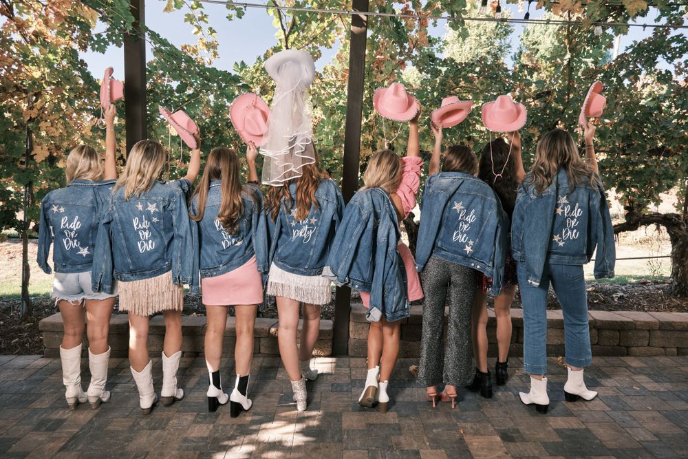 A group wearing matching denim jackets poses with pink balloons outdoors.