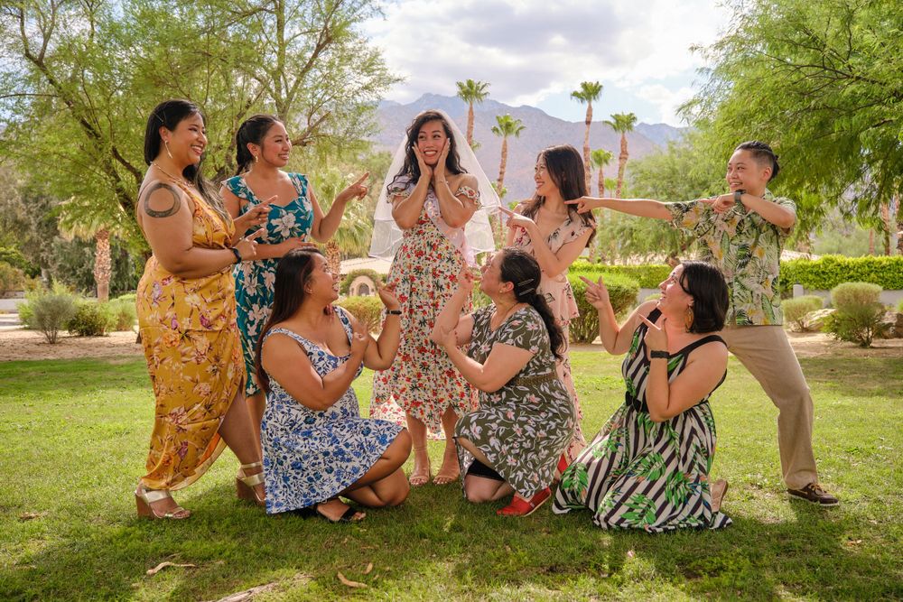 A playful group poses for a photo on grass with palm trees in the background.