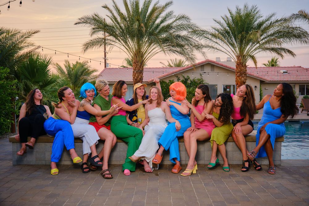 A fun group photo of friends in colorful outfits sitting in a row outdoors.