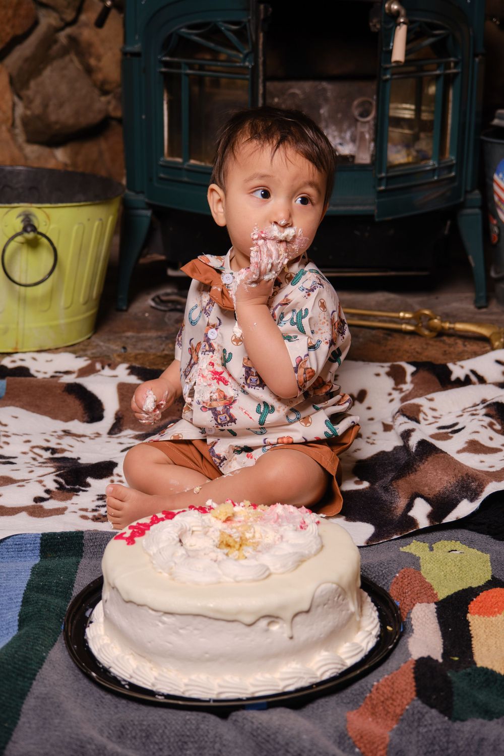 A small child in floral attire enjoying a white frosted birthday cake.