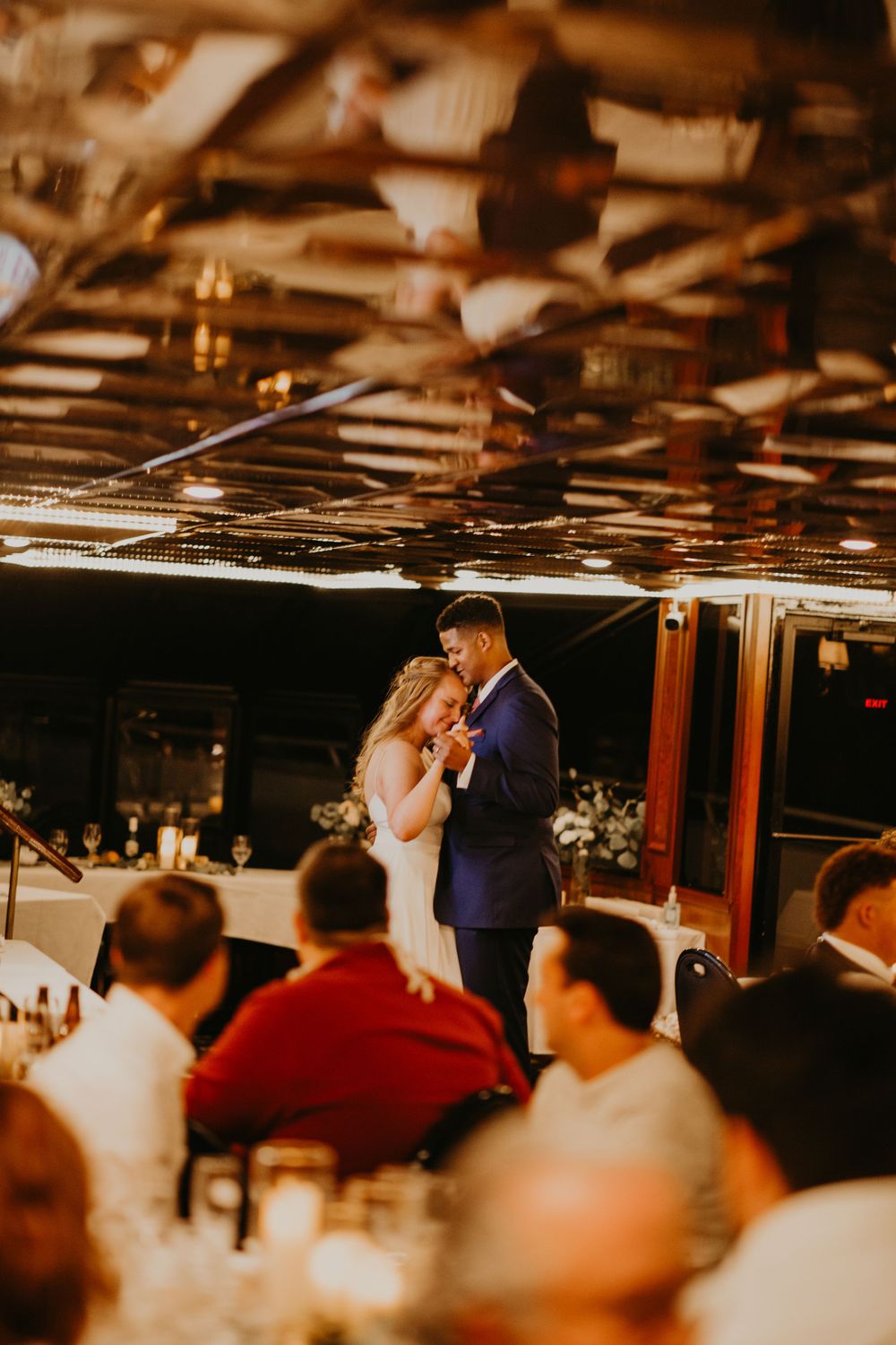Bride and groom dancing closely as wedding guests watch from decorated reception tables.