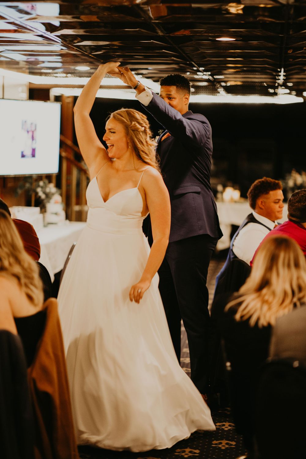 Bride laughing joyfully as groom twirls her during energetic wedding reception dance.