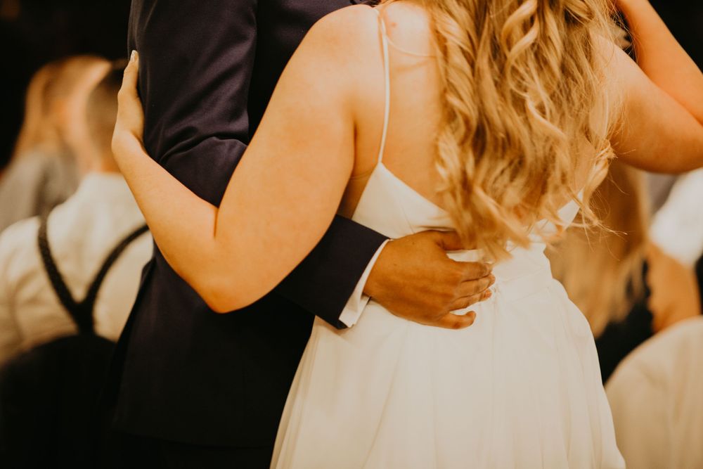 Close-up of groom's hand on bride's waist during romantic wedding reception dance.
