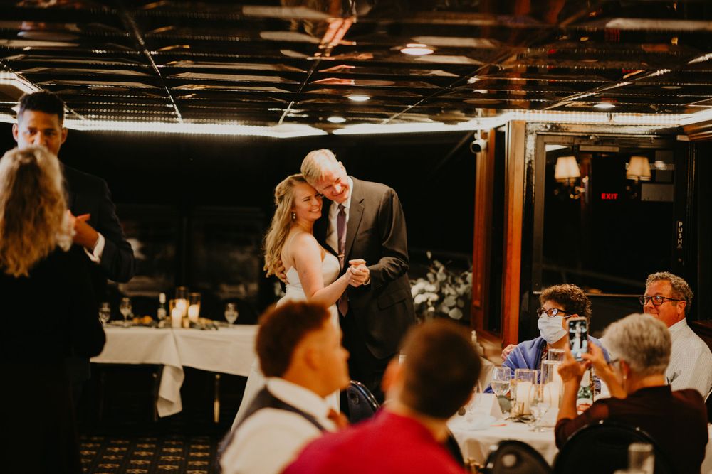 Bride shares a tender father-daughter dance at warmly lit wedding reception.