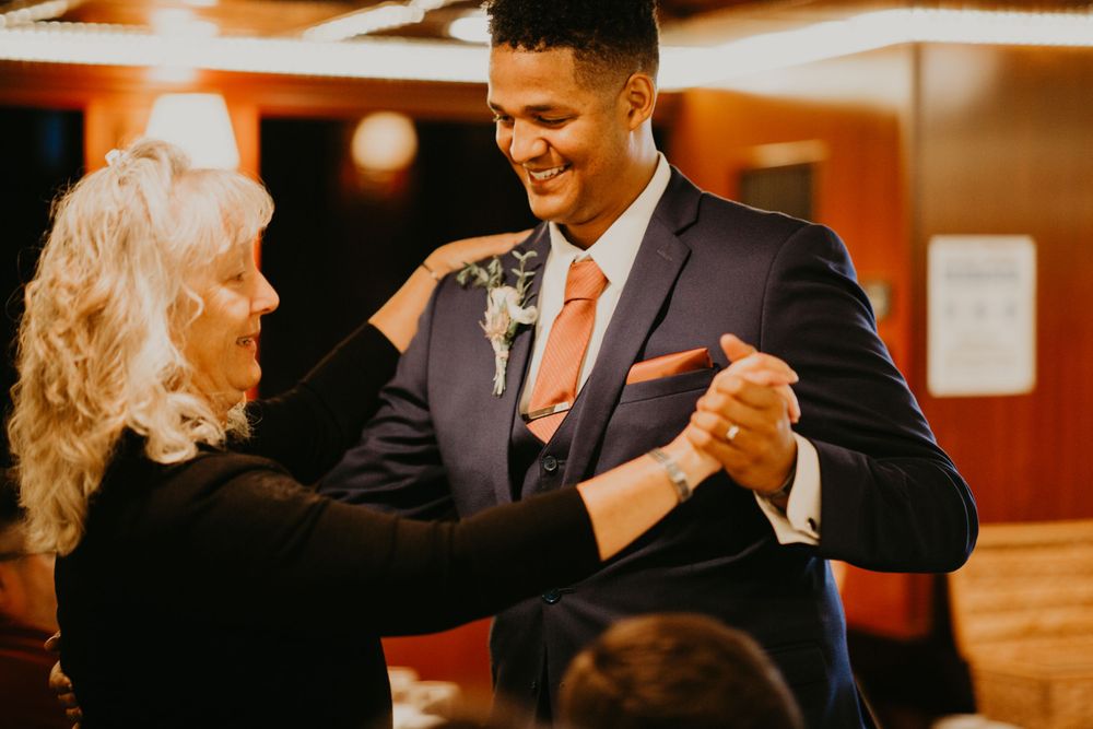 Smiling groom shares a joyful mother-son dance at wedding reception celebration.
