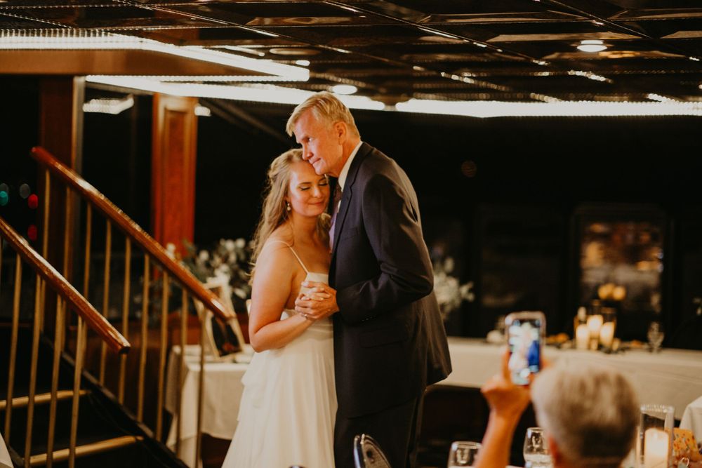Bride and father share a tender father-daughter dance at a warmly lit wedding reception.