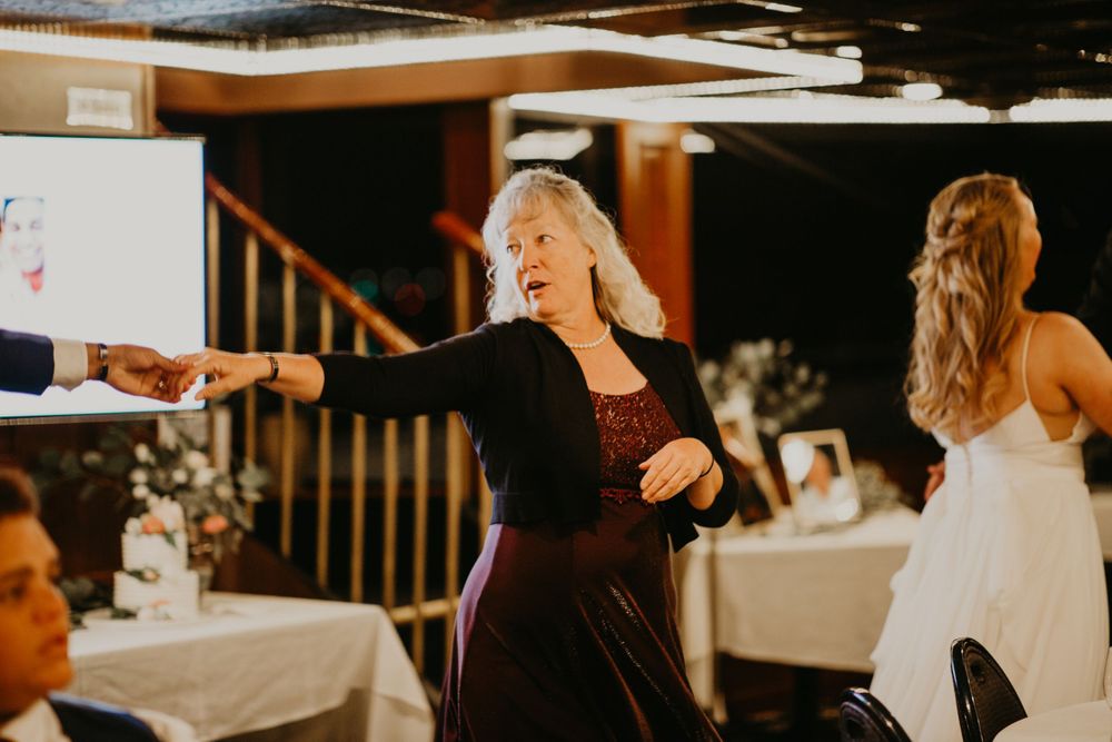 Elegant wedding guest in black cardigan dances joyfully at a reception venue.