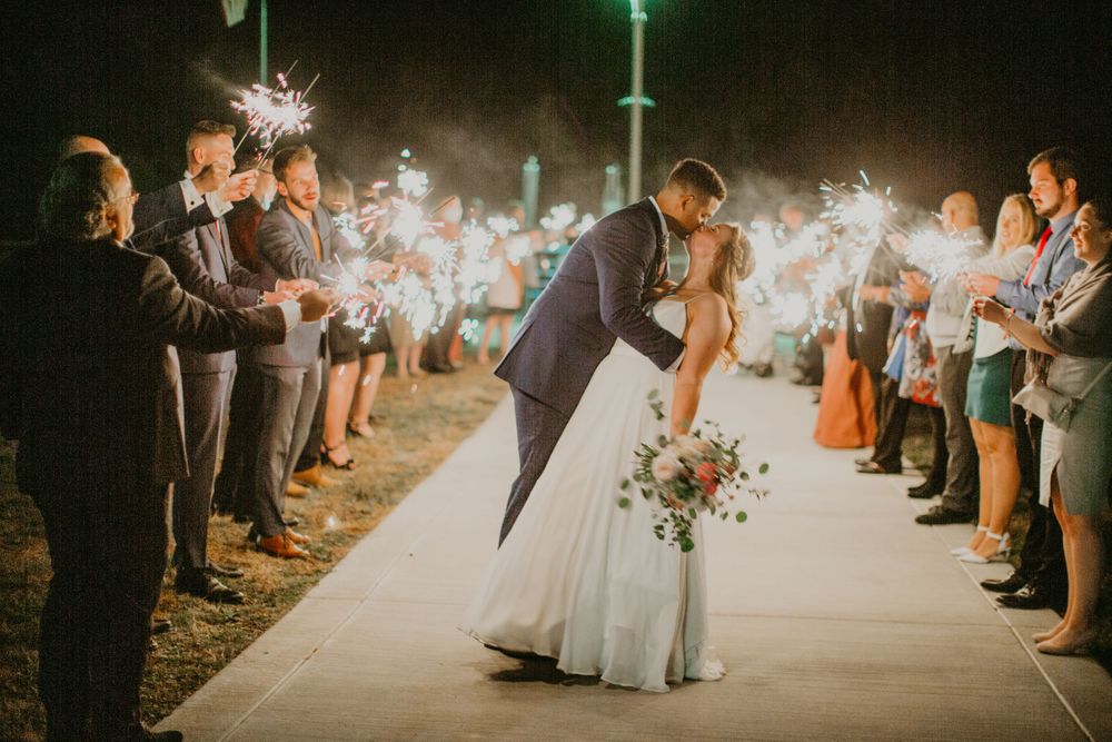 Bride and groom share a romantic dip kiss during a dazzling sparkler send-off at night.