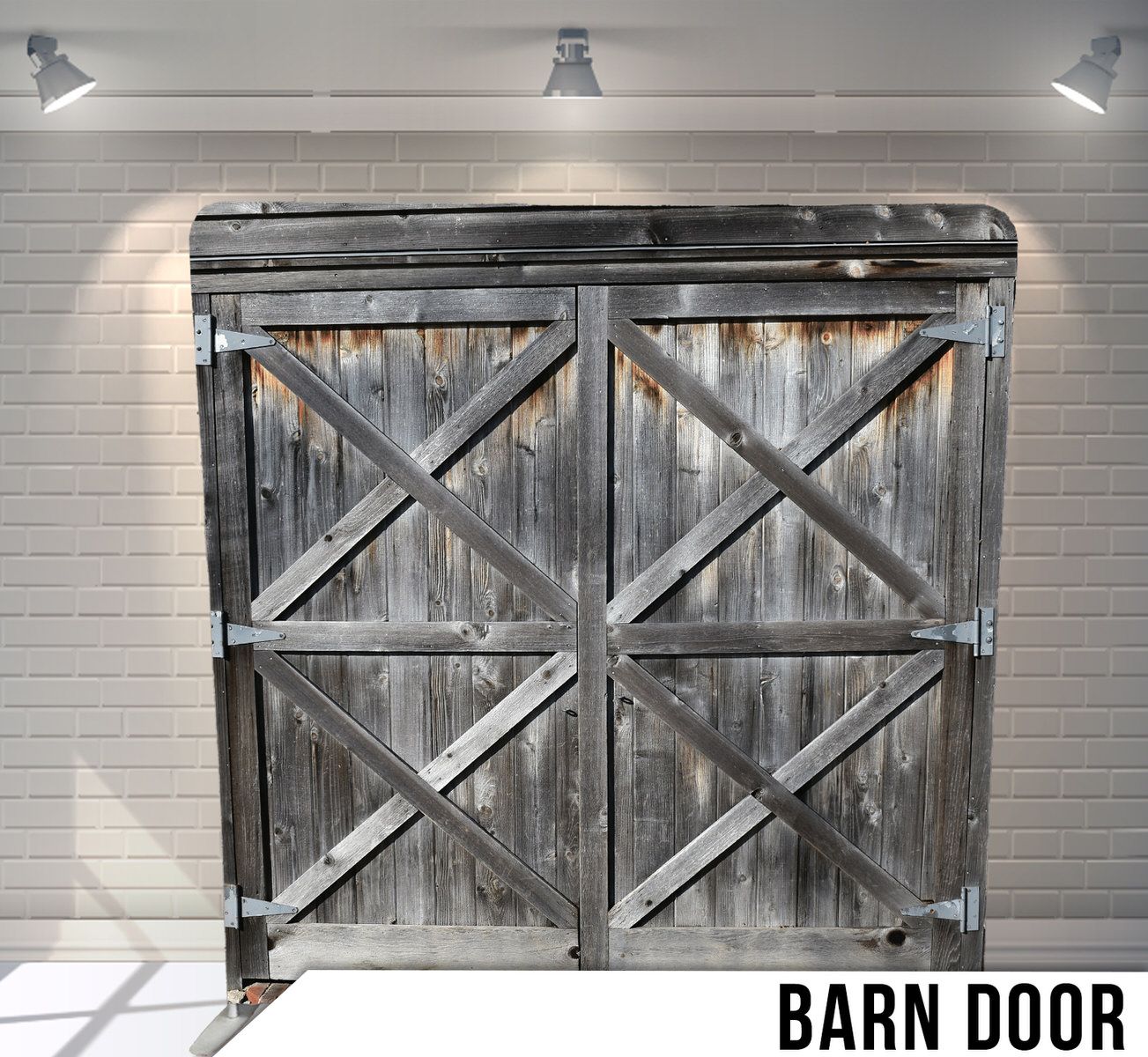 Weathered rustic barn door with X-frame design and metal hardware mounted on white brick wall.
