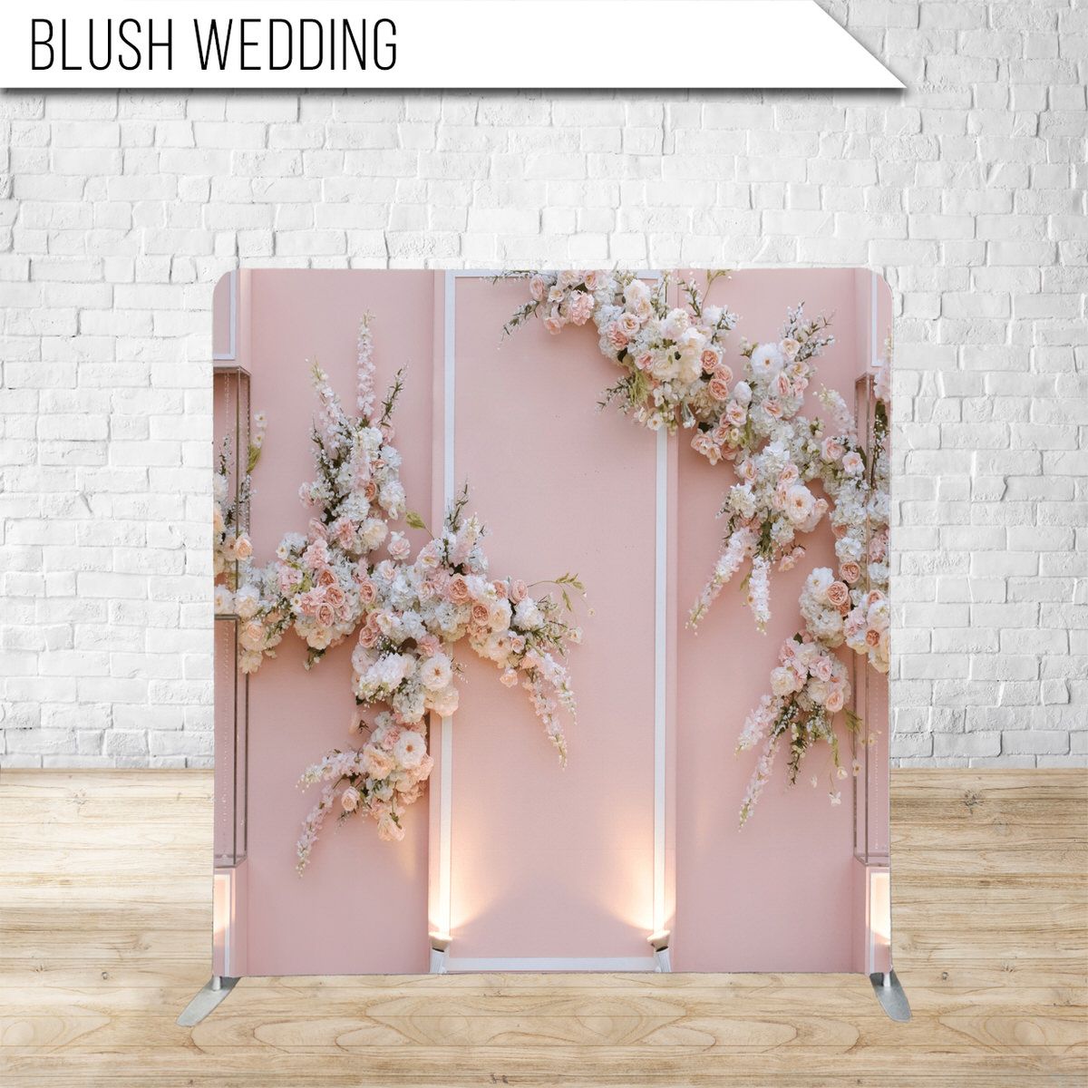 Elegant blush pink wedding backdrop with romantic floral arrangements and soft lighting against a white brick wall.