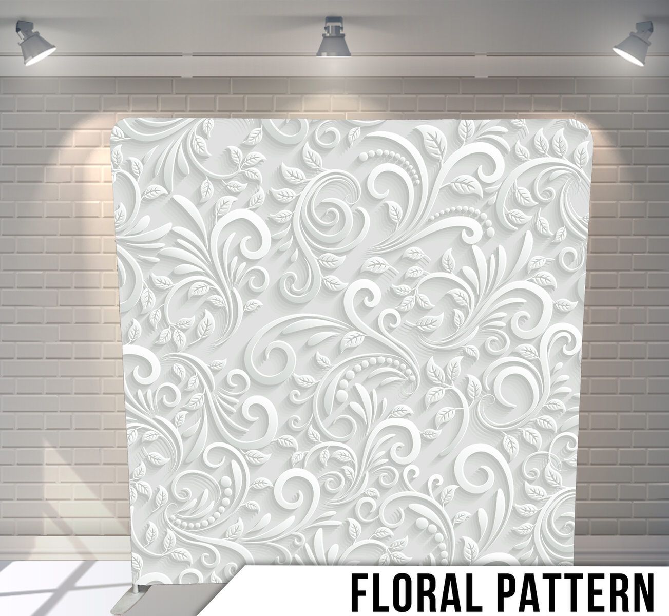 A white decorative floral pattern backdrop with swirling baroque designs illuminated by spotlights on a stage.