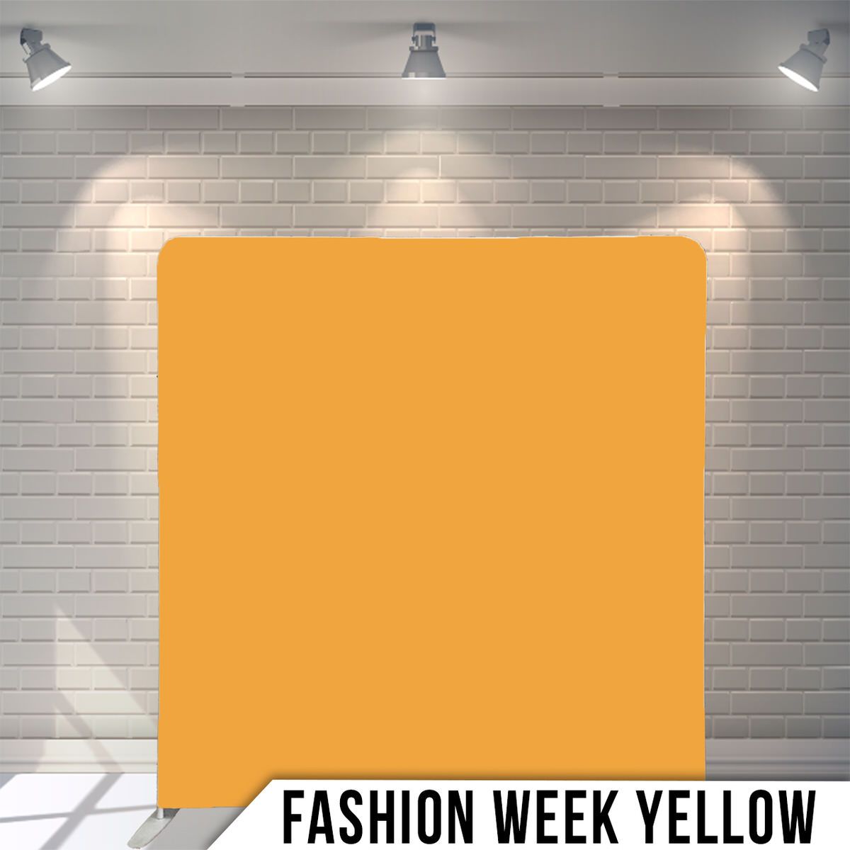 A bright yellow backdrop panel illuminated by spotlights against a white brick wall for fashion week photography.