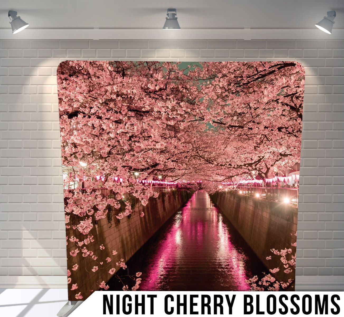 Pink cherry blossoms illuminated at night along a canal with reflections in the dark water.