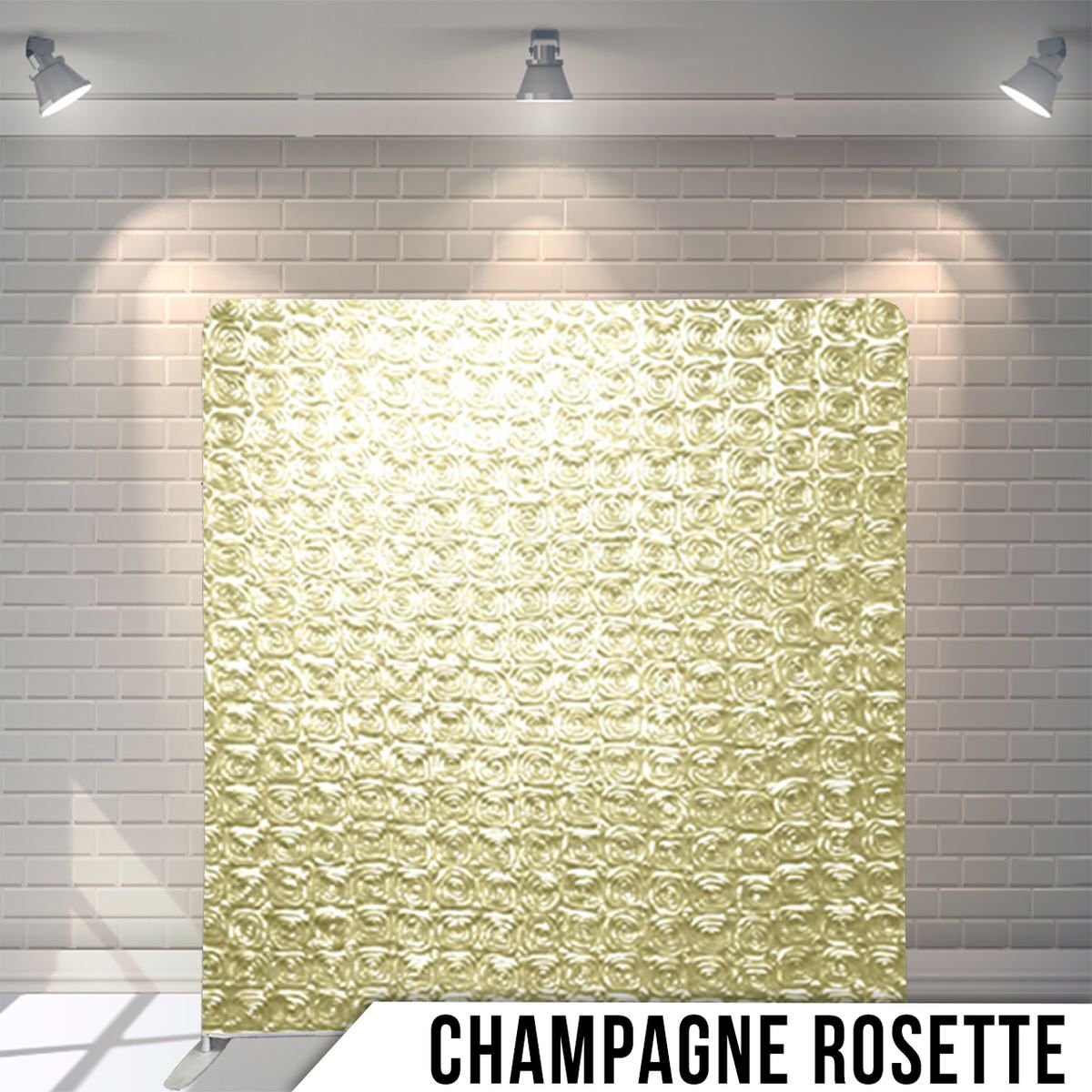 Textured champagne-colored rosette fabric backdrop illuminated by overhead spotlights against white brick wall.