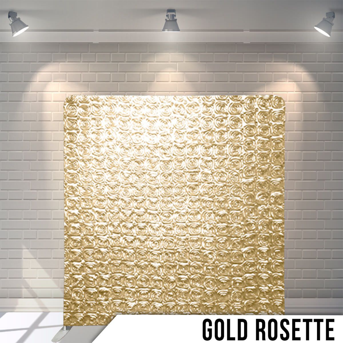 Metallic gold rosette textured backdrop panel illuminated by overhead lights against white brick wall.
