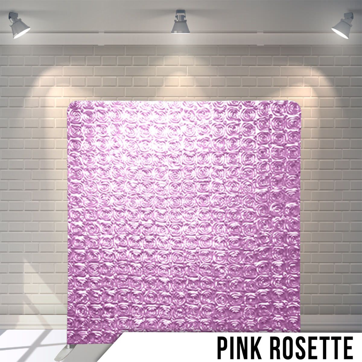 Soft pink rosette patterned fabric backdrop illuminated against white brick wall background.