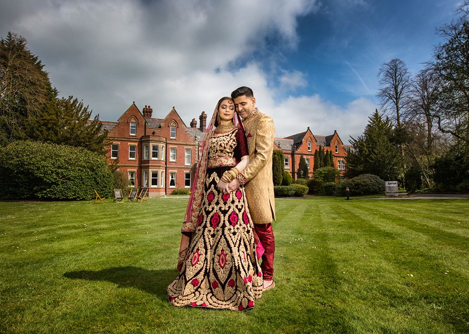 Asian bride and groom stand and embrace on the grass lawn of the Preston Marriott Hotel in Summer