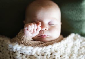 Sleeping newborn with hand near face resting on cream knit blanket.