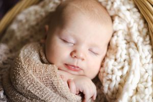 Peaceful sleeping newborn wrapped in beige knit blanket.