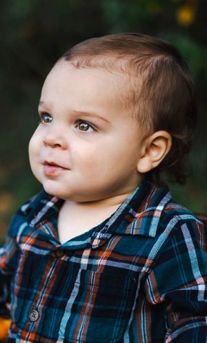 Baby in a plaid shirt gazing to the side with bright eyes and rosy cheeks.