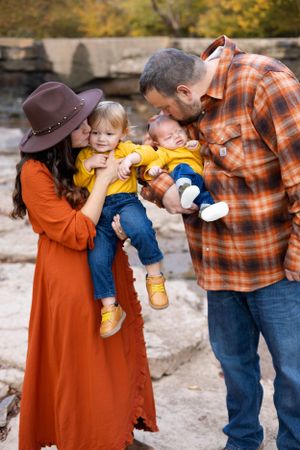 Family in autumn attire shares playful moment on stone surface outdoors.