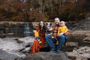 Family of four sits together on rocky outcrop near waterfall during autumn.