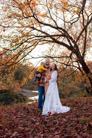 Couple poses outdoors in autumn with a lace wedding dress and flannel shirt amid falling leaves.