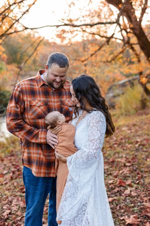 Couple with baby enjoying autumn foliage in rustic outdoor setting.