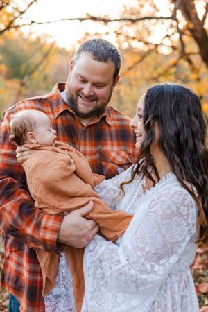 Family sharing an intimate moment outdoors during autumn with baby in brown outfit.