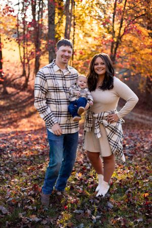 A family poses together in coordinating plaid outfits among fall foliage in the woods.