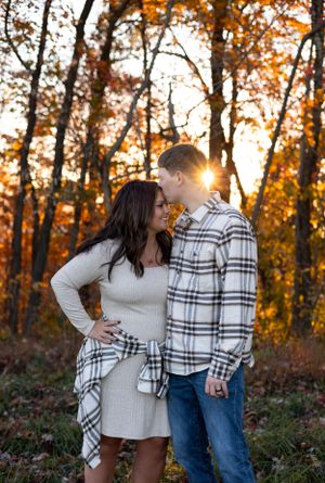 Romantic couple embracing in autumn forest with golden sunlight filtering through trees.