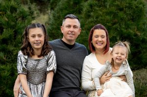 Family of four poses together against a backdrop of evergreen trees.