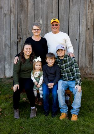 A multigenerational family group poses together against a weathered wooden barn background.