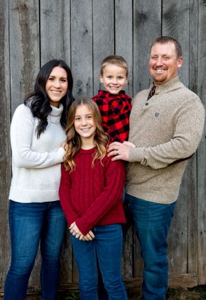 Family of four poses against weathered wooden wall wearing coordinated sweaters.