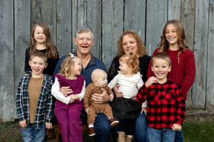 Large family group poses together in front of rustic wooden barn wall wearing casual plaid shirts.