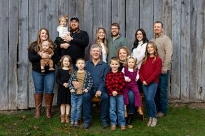 A large family group poses together against a rustic wooden barn wall wearing coordinated fall outfits.