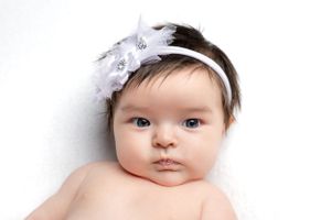 Baby wearing white floral headband against white background.