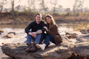 Couple sitting together on rocky outcrop during sunset in casual autumn attire.