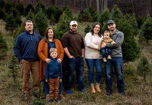 Family poses together in casual clothing at a Christmas tree farm during winter.